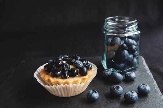 Blueberry tart on a dark background. Blueberry cupcake on black serving board with scattered berries