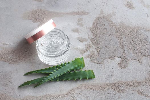 Gel texture with bubbles hyaluronic acid and aloe vera branches in a glass jar on a concrete background