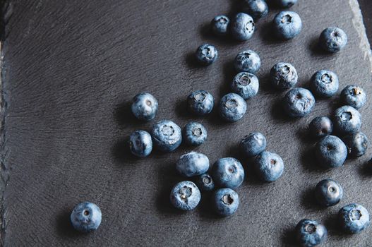 Blueberries scattered on a black background of natural stone. Still life with wild berries on a black background.