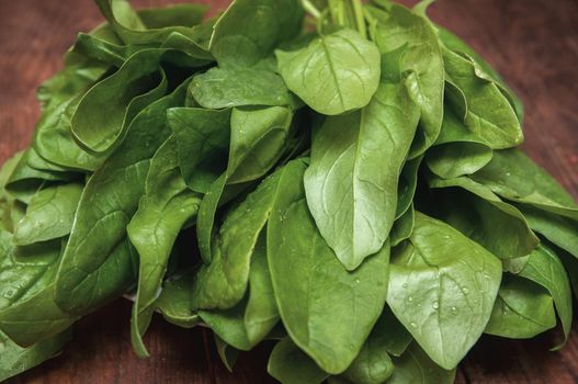 bunch of fresh spinach lies on a brown wooden table