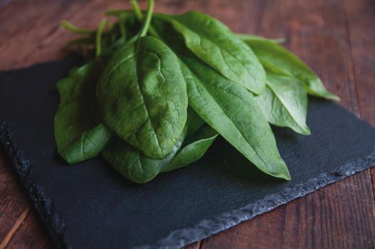 fresh spinach lies on a black presentation board located on a brown wooden table