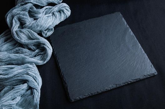 Black slate board on top view of dark stone texture with gray gauze tablecloth. Empty space for a menu or recipe