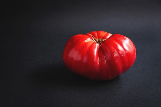 Huge big red tomato on a black serving board on a dark background