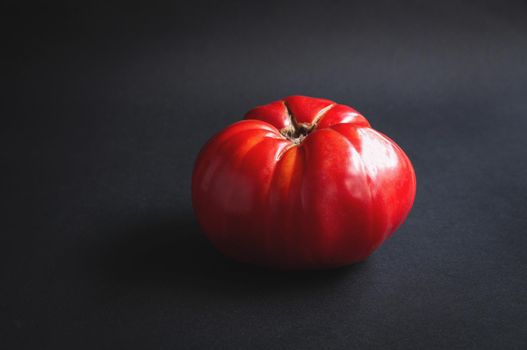 Huge big red tomato on a black serving board on a dark background