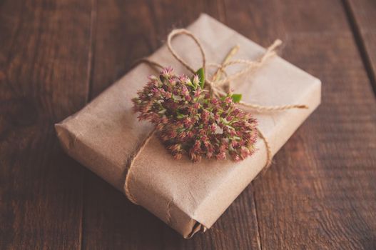 Homemade wrapped present in kraft paper and pink flowers on a wood table. Close-up image of beautiful gift box decorated with flowers