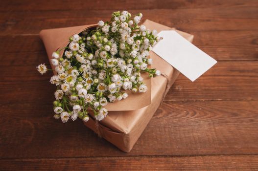 gift is wrapped in craft paper, next to it is a bouquet of chamomile flowers lying on a wooden table