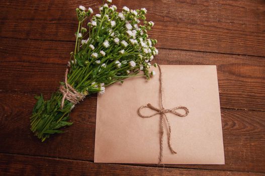 envelope made of craft paper, next to a bouquet of chamomile flowers, which lies on a wooden table