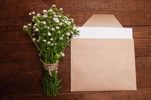 envelope made of craft paper, next to a bouquet of chamomile flowers, which lies on a wooden table