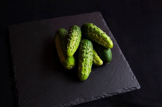 Natural fresh green cucumbers from a home garden on a black background, a dummy board made of stone. View from above.