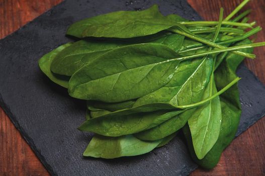 fresh spinach lies on a black presentation board located on a brown wooden table