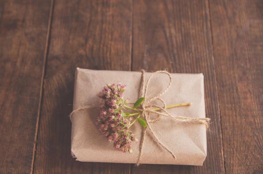 Homemade wrapped present in kraft paper and pink flowers on a wood table. Close-up image of beautiful gift box decorated with flowers