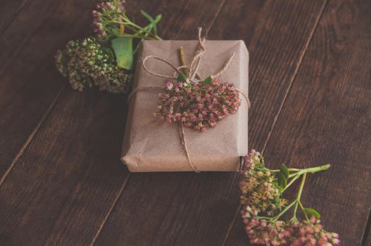 Homemade Gift box wrapped in kraft paper and pink flowers on wooden table