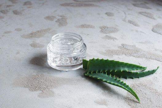 Gel with hyaluronic acid and aloe vera branches in a glass jar on a concrete background