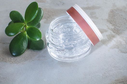 Gel texture with bubbles hyaluronic acid and aloe vera branches in a glass jar on a concrete background