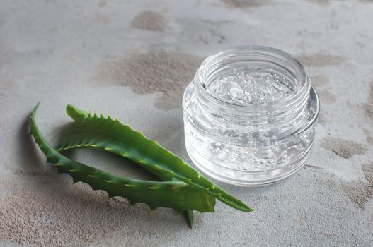 Gel texture with bubbles hyaluronic acid and aloe vera branches in a glass jar on a concrete background