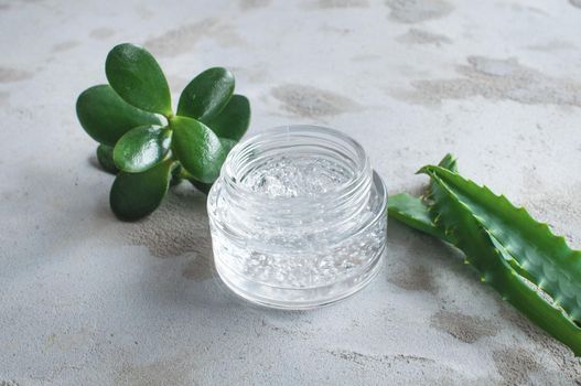 Gel texture with bubbles hyaluronic acid and aloe vera branches in a glass jar on a concrete background