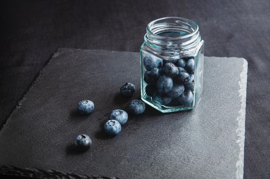 Fresh blueberries in a glass jar and laid out on a black board. Blueberries for a healthy diet and vegetarians