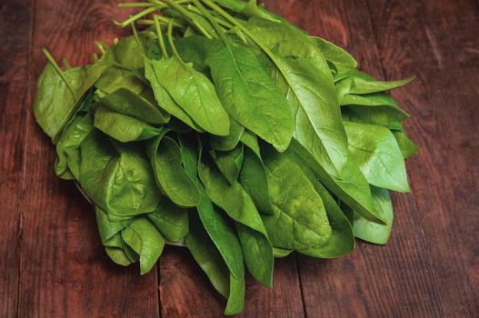 bunch of fresh spinach lies on a brown wooden table