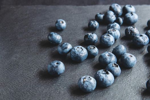 Blueberries scattered on a black background of natural stone. Still life with wild berries on a black background.