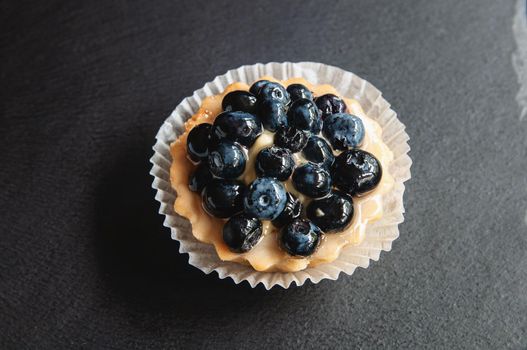 Tart with blueberries is on a black background of natural stone. Still life with sweet cakes with wild berries on a dark background