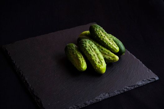 Natural fresh green cucumbers from a home garden on a black background, a dummy board made of stone. View from above.