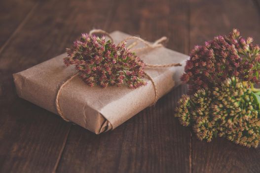 Homemade Gift box wrapped in kraft paper and pink flowers on wooden table