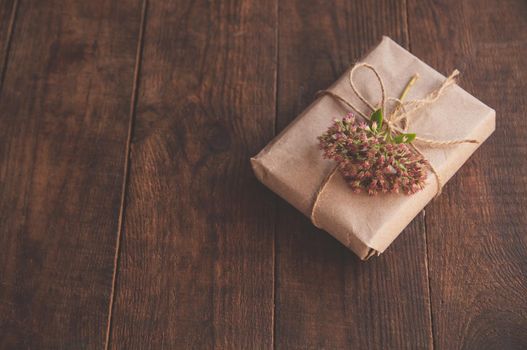 Homemade wrapped present in kraft paper and pink flowers on a wood table. Close-up image of beautiful gift box decorated with flowers