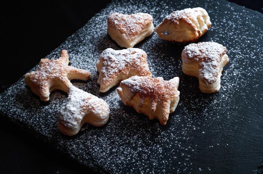 tasty background of cinnamon cakes from puff pastry  on a black slate background, sprinkled with powdered sugar