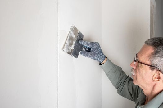 Adult man makes even and putty the corners in his house with special mixture. Home renovation, DIY concept. Selective focus.