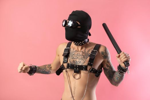 the balaclava man with leather straps on his body for bdsm sex toys with a rubber baton in his hands