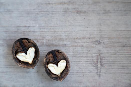 Two halves of split walnut with core in form of white hearts on wooden background. Concept of Valentine's Day and health. Copy space.