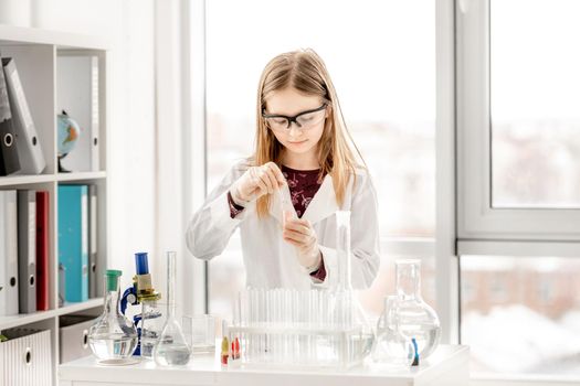 Smart girl doing scientific chemistry experiment wearing protection glasses. Preteen schoolgirl with equipment and chemical liquids on school lesson