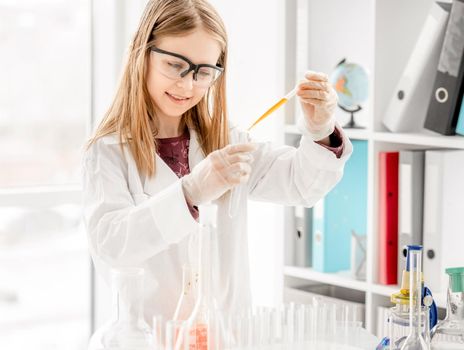 Girl doing scientific chemistry experiment wearing protection glasses and measuring liquid. Schoolgirl with test equipment on school lesson