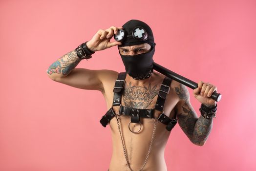 the balaclava man with leather straps on his body for bdsm sex toys with a rubber baton in his hands