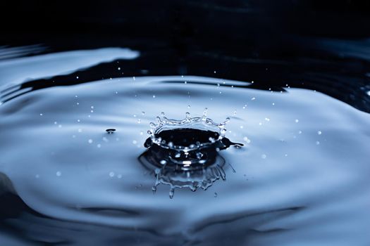 Crown from a splash of water on a dark background. Liquid background with glitter. Small waves. Selective focus.