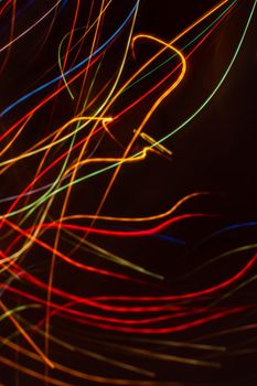Drawing with light. Abstract multicolored rays on a black background. Curved wave lines. Vertical background.