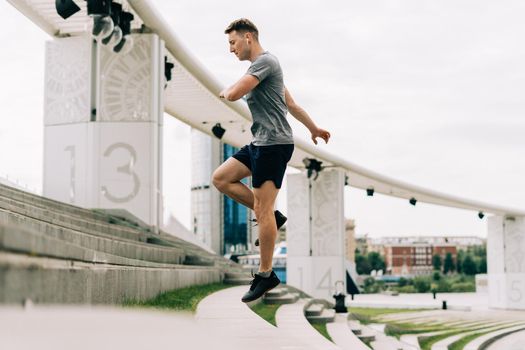 Young athlete man runner running up and down on city stairs in summer on morning run, background urban city street. Sports training. Fitness cardio workout in fresh air, jumping outside.