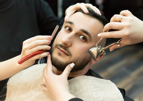 man in a men's barber shop is served by two pairs of hands shaving his beard