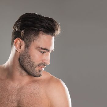 Portrait of handsome young naked man with stylish haircut and bristle over gray background