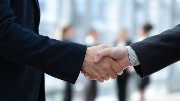 Business handshake and business people in office on background