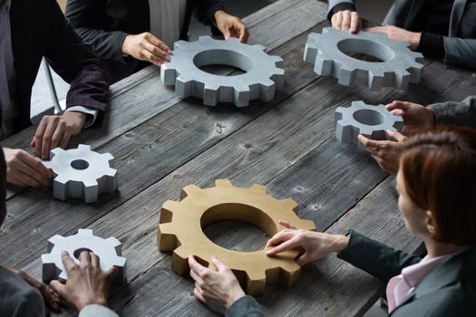 Group of businesspeople joining together gears on table at workplace