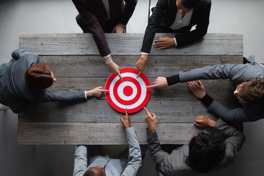 Team of business people pointing at red target at meeting table