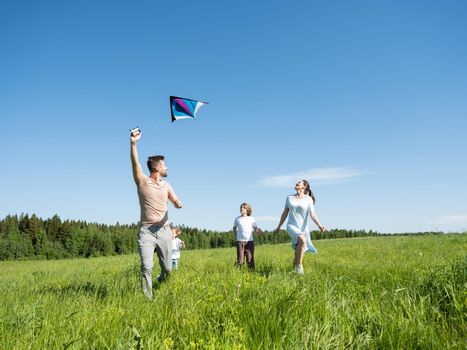 Family of parents and children running through field letting kite fly