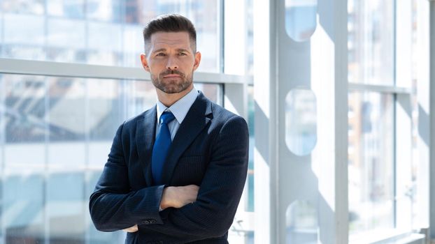 Mid adult businessman standing in office with arms folded looking at the camera