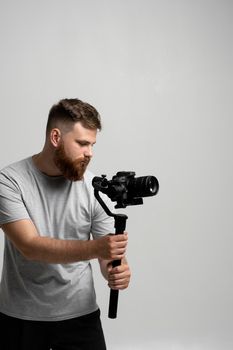 Professional male videographer filmmaker cinematographer dop shooting video using modern dslr camera on 3-axis gimbal over white wall