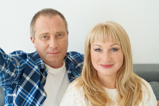 Self-portrait of mature couple in home interior on sofa. Handsome man and attractive middle-aged woman enjoy spending time together taking selfie