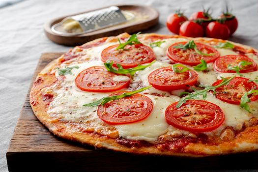 Rustic Italian homemade Pizza Dough margherita topped with pizza sauce from canned tomatoes, mozzarella cheese and arugula on dark linen textile tablecloth, side view