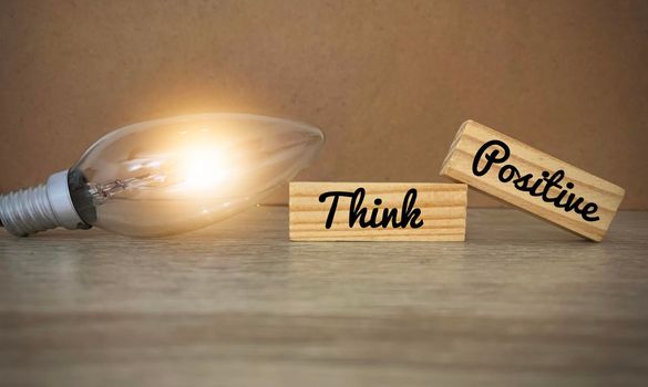 Image photo with words"Think Positive" on wooden blocks with shinning bulb. Close up