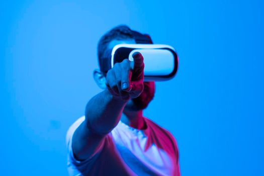 Attractive bearded man experiencing with virtual reality with VR headset and trying touching something with his hands what he see in front of him in cyberspace. Metaverse and gaming concept