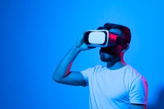 Closeup of young man wearing virtual reality goggles in modern studio with a neon light. Smartphone using with VR headset. Future technology concept